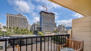 A balcony with wooden furniture and a view of a cityscape including a building under construction.
