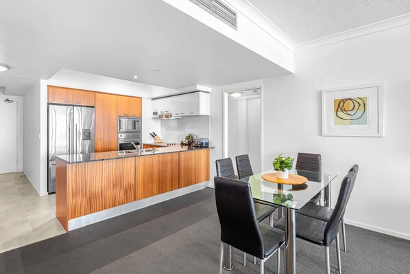 A modern kitchen with a central island, a dining area with a glass table and black chairs, and a framed abstract painting on the wall.