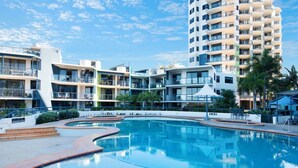 Un hotel con piscina, varios balcones y un edificio alto al fondo.