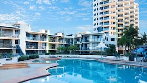 A hotel with a swimming pool, multiple balconies, and a tall building in the background.