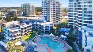 A modern hotel complex with multiple high-rise buildings, a central swimming pool, and surrounding greenery.