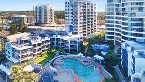 A modern hotel complex with multiple high-rise buildings, a central swimming pool, and surrounding greenery.