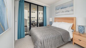 A hotel room with a bed, a nightstand, a lamp, a painting, and a view of the outside balcony.