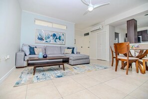 A living room with a grey sofa, a coffee table, and a dining area with wooden chairs.