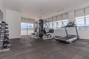Une salle de sport équipée d’un tapis de course, d’un banc de musculation et d’haltères.