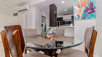 Un coin repas avec une table en verre, quatre chaises et un tableau accroché au mur.