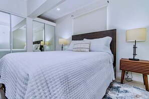 A modern bedroom with a large bed, bedside lamps, a wooden nightstand, and a glass closet.