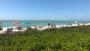 A beach with people relaxing under colorful umbrellas, a clear sky, and a view of the ocean. - 8M Dollar Home, 3 Houses from Beach in Old Naples! (Naples)