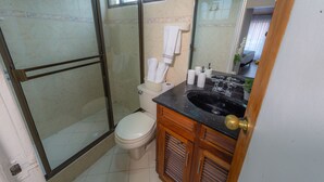 A bathroom with a glass-enclosed shower, a toilet, and a sink with a wooden cabinet. - Modern Loft in Chapinero Alto (Bogotá)