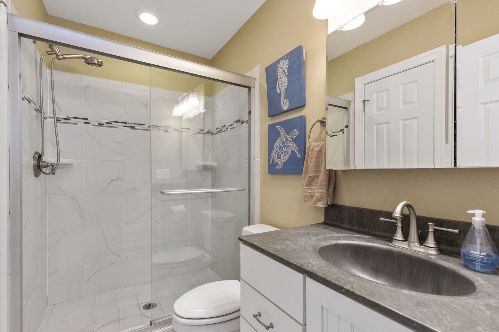 A modern bathroom with a glass-enclosed shower, a white toilet, a sink with a faucet, and a mirror above the sink.