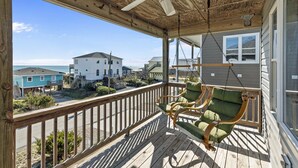 Una terrazza in legno con una ventola a soffitto, una sedia a dondolo e vista sulle case e sull'oceano.