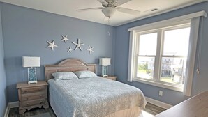 Camera da letto con un letto, comodini, una ventola a soffitto, decorazioni a tema stelle marine e una finestra con vista sugli edifici.