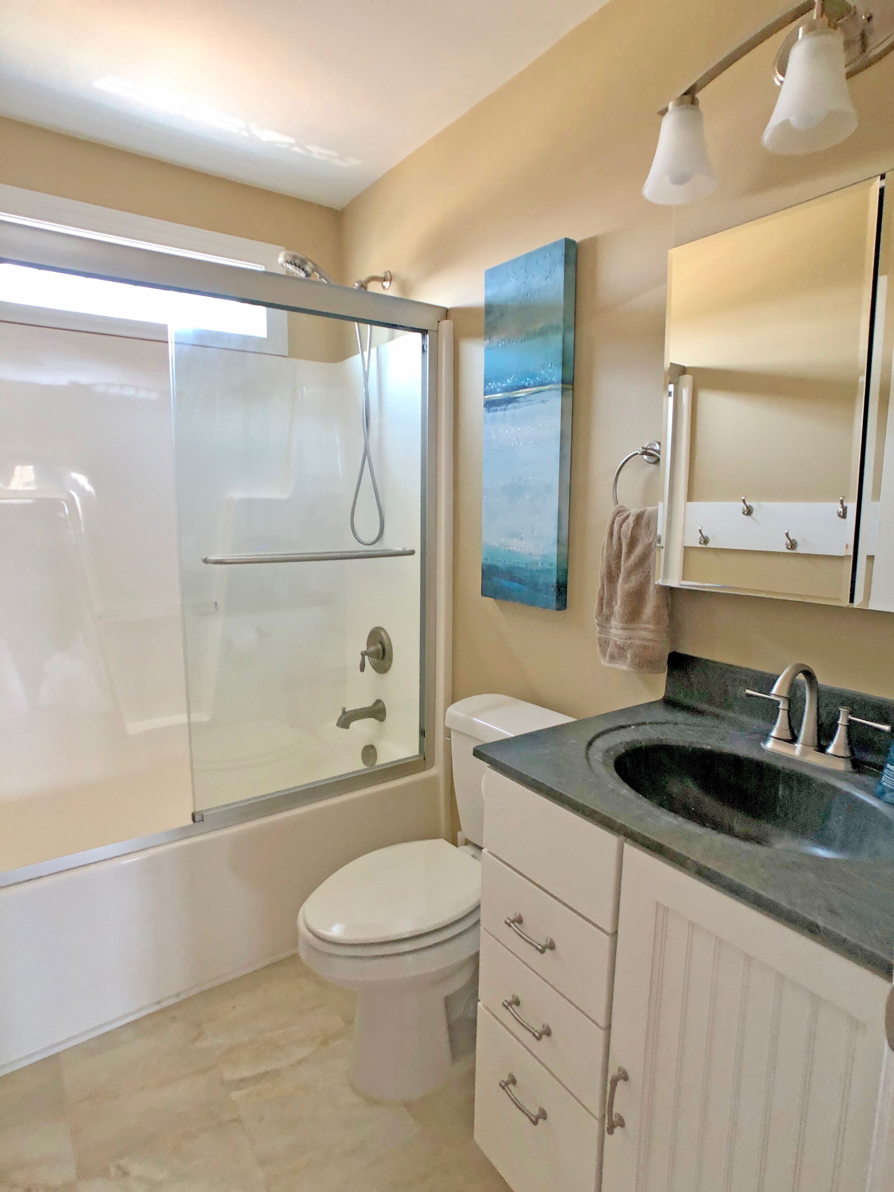 Une salle de bain avec une douche à parois de verre, des toilettes, un lavabo avec un miroir au-dessus et une serviette suspendue à un porte-serviettes.