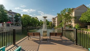 A wooden deck with benches overlooking a water body, surrounded by a metal fence and buildings.