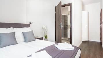 A modern hotel room with a large bed, a wooden wardrobe, and a bathroom visible through an open door.