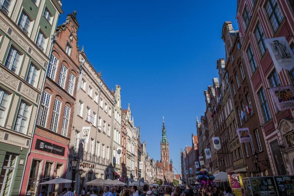 A bustling street with historic buildings, a prominent clock tower, and various shops.