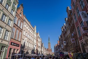 A bustling street with historic buildings, a prominent clock tower, and various shops. - Black Swan House (Gdansk)