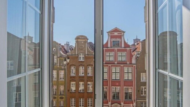 A view through a window of a building with multiple stories, featuring traditional architecture with red and yellow facades. - Black Swan House (Gdansk)