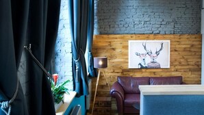 A room with a brick wall, a wooden panel wall, a purple leather sofa, a floor lamp, and a framed picture of deer. - Black Swan House (Gdansk)