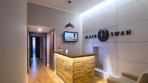 A reception area with a wooden reception desk, a mounted television, and a wall-mounted sign reading "BLACK SWAN". - Black Swan House (Gdansk)