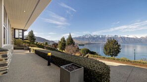 A modern building with a stone facade, a paved walkway, and a view of a lake with mountains in the background. - Q by the Lake Aspen Grove Stunning Views (Queenstown)