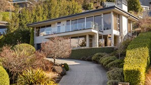 Une maison moderne à deux étages, dotée d’un balcon, entourée de jardins bien entretenus et agrémentée d’une allée pavée.