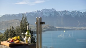 Een prachtig uitzicht op een meer met bergen op de achtergrond, een eettafel met eten en een wijnglas, en een telescoop op de voorgrond.