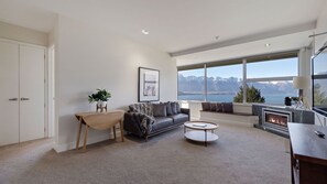 Un salon moderne avec un canapé, une table basse et une cheminée, donnant sur un paysage montagneux.