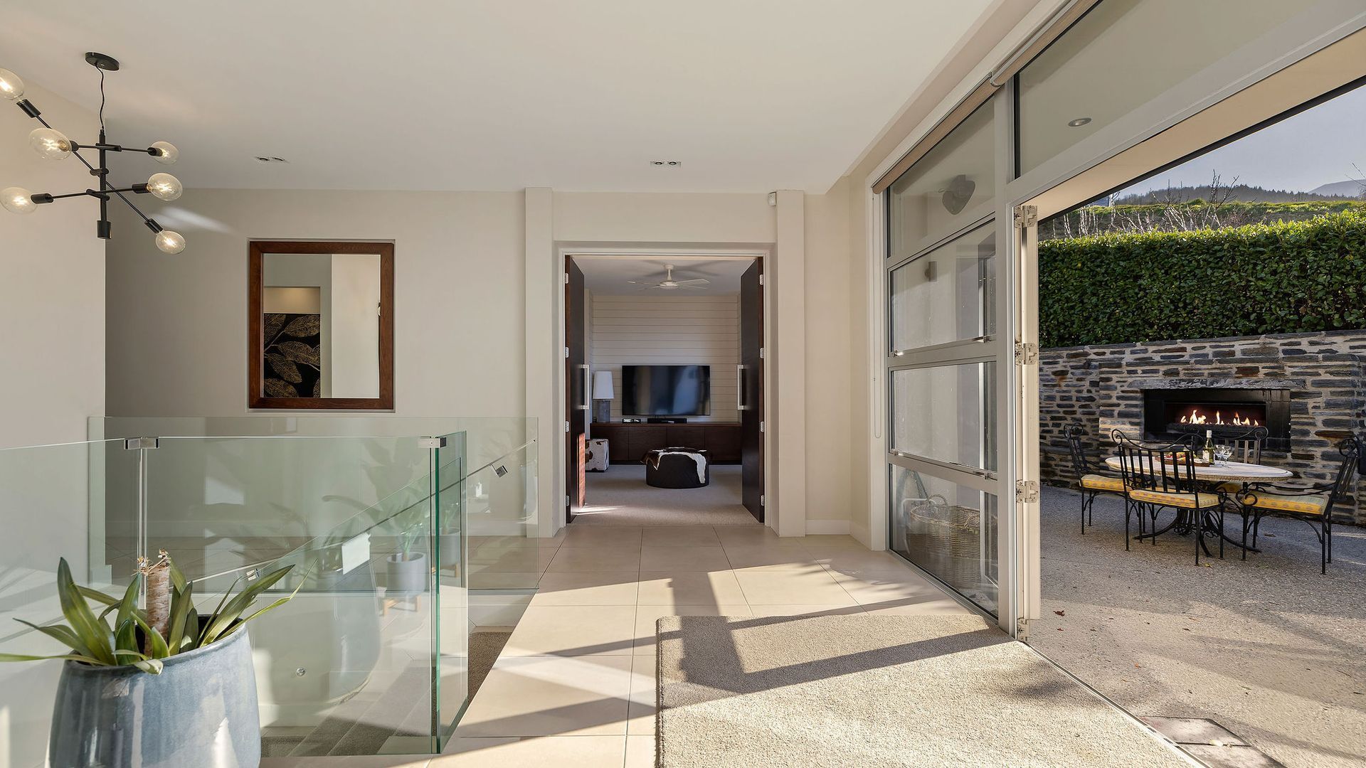A modern interior with a glass railing, a flat-screen TV, and a stone fireplace.