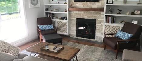Una sala de estar con chimenea, televisor montado en la pared y estantería.