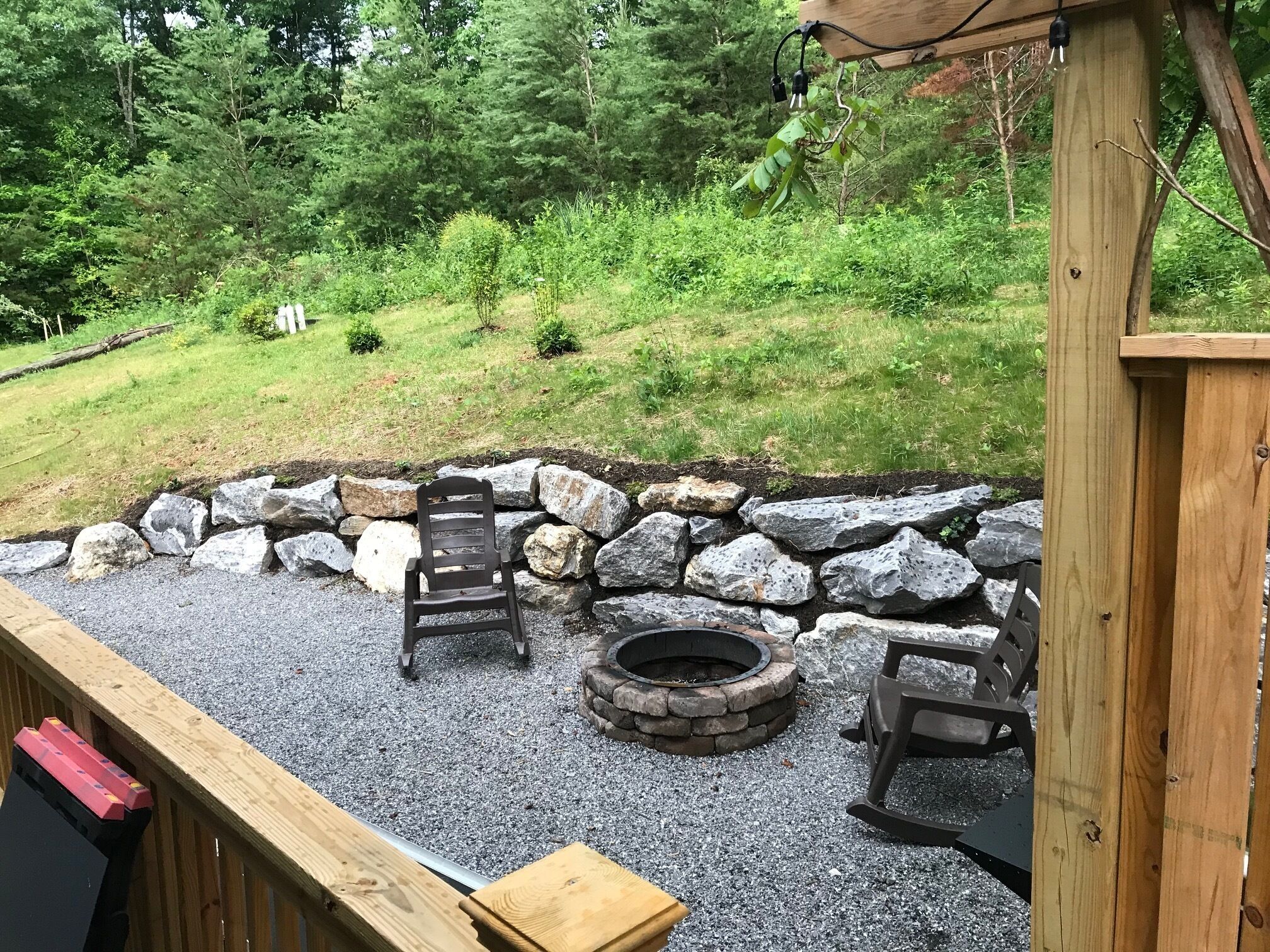 Une terrasse avec un foyer en pierre, deux chaises en bois et une table en bois.