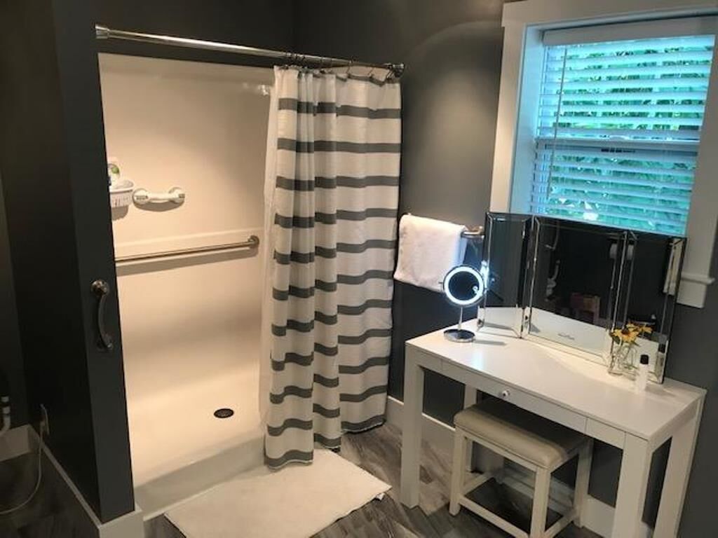 A bathroom with a shower, a vanity with a mirror, and a window with blinds.