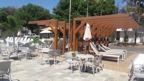 A poolside area with lounge chairs and tables, a wooden pergola, and umbrellas. - International Resort (Chácara Roma)