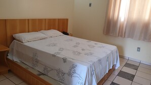 A single bed with a wooden headboard, a bedside table with a phone, and a wall-mounted air conditioner. - International Resort (Chácara Roma)
