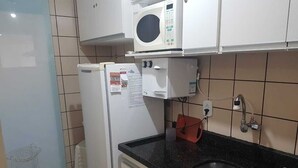 A compact kitchen with a refrigerator, microwave, and a sink. - International Resort (Chácara Roma)