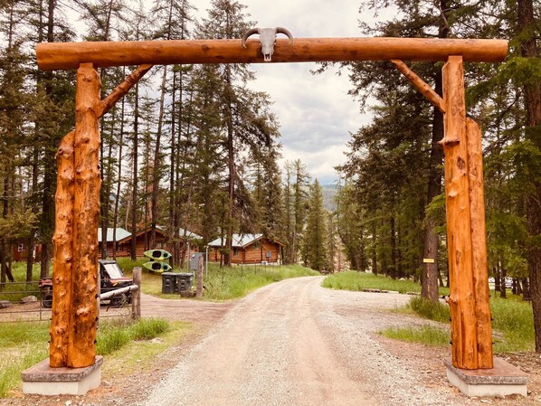 A rustic wooden archway leading to a cabin in a forested area.