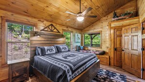 Un dormitorio de cabaña de madera con una cama, un ventilador de techo y una ventana con persianas.