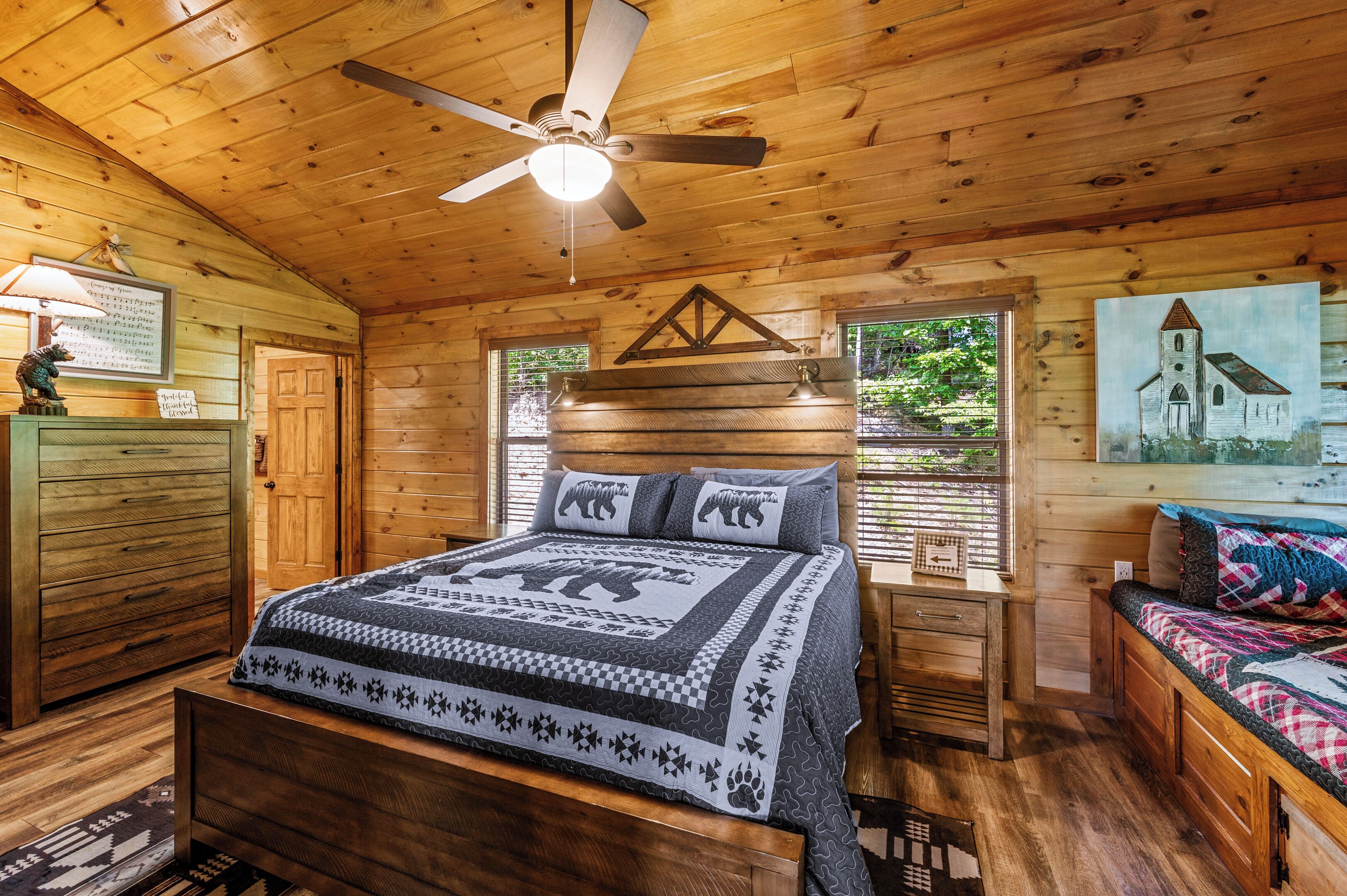 Une chambre à coucher dans une cabane en bois, avec un lit, une table de chevet, une commode et un ventilateur de plafond.