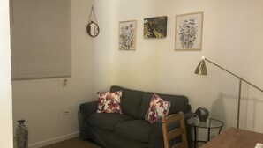 A living room with a grey sofa, two floral cushions, a round mirror, and three framed artworks on the wall. - Beautiful Apartment at Miramar (Santurce)