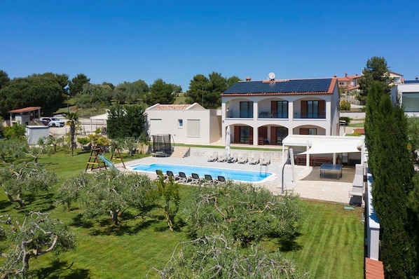A large house with a swimming pool, outdoor seating, and a tennis court.