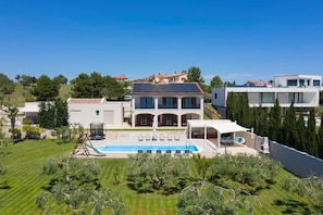 A modern villa with a swimming pool, outdoor seating, and a view of the surrounding landscape.