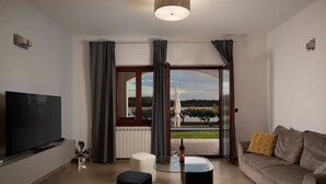 Een moderne woonkamer met een flatscreen televisie, een bank, een glazen salontafel en uitzicht op een meer door grote ramen.