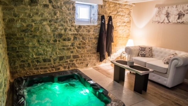 Une pièce aux murs de pierre, équipée d’un jacuzzi, d’un canapé et d’une petite table.