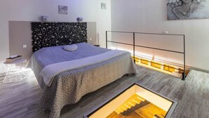 Une chambre moderne avec un grand lit, une tête de lit décorative, une table de chevet et un revêtement de sol original.