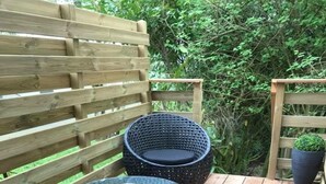 Une terrasse en bois agrémentée de meubles en osier, notamment deux tables rondes et deux chaises.