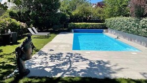 A swimming pool with a clear blue water, surrounded by a well-maintained garden and a statue.