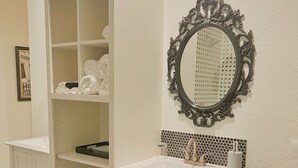 A bathroom with a white vanity, a mirror with an ornate frame, and a tiled backsplash.