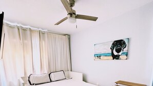 Une chambre à coucher avec un lit, un bureau, une chaise, un ventilateur de plafond et un tableau accroché au mur.