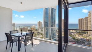 A balcony with a glass table and chairs, overlooking a cityscape and the ocean. - Circle on Cavill Ocean & River Views (Surfers Paradise)