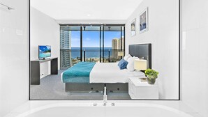 A modern bedroom with a large bed, a TV, a bathroom, and a view of the ocean. - Circle on Cavill Ocean & River Views (Surfers Paradise)